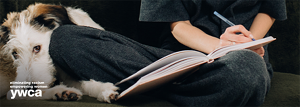 Woman sitting down on the couch with her dog next to her writing down her goals in a journal
